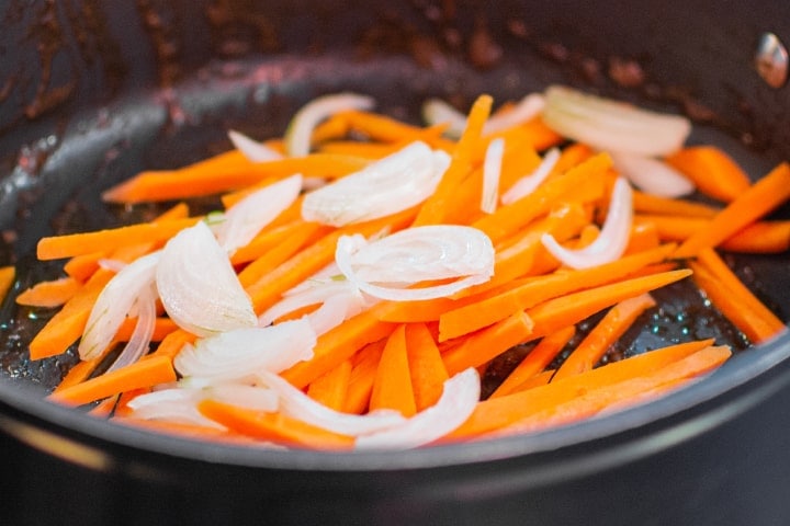 Frying carrots and onions into a pan