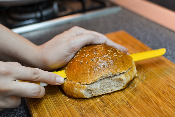 Cutting the burger buns into a half on a cutting board.