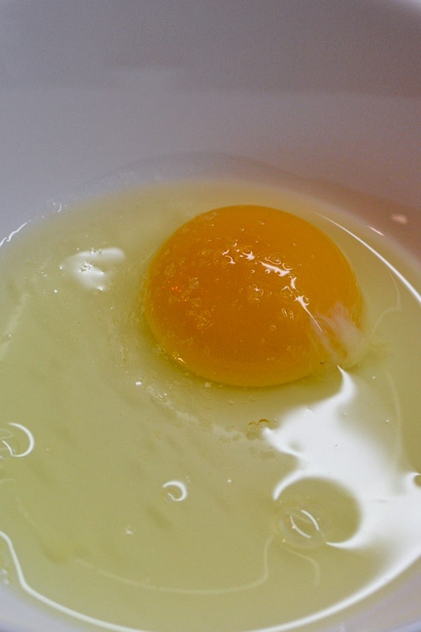 Mixing a raw egg with salt in a white plate.