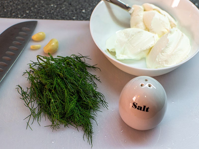 Dill with sour cream and garlic on a white cutting board.