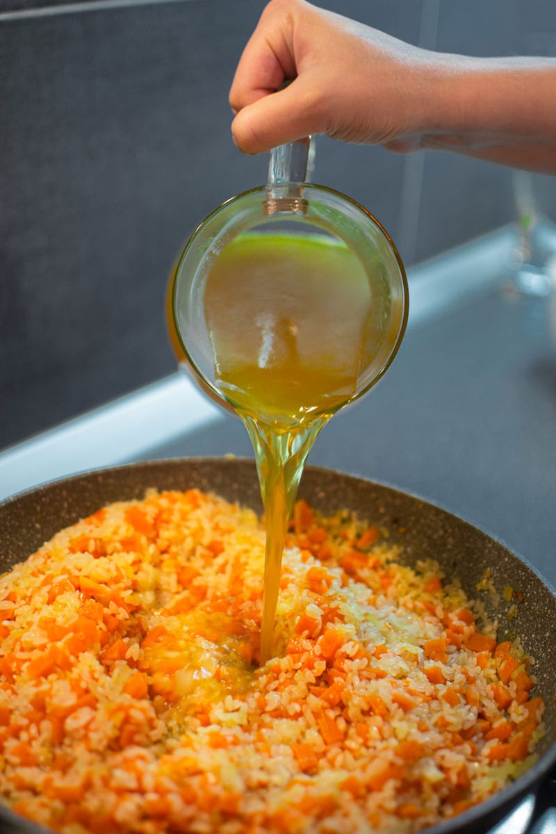 Pouring meat broth in a pumpkin risotto.