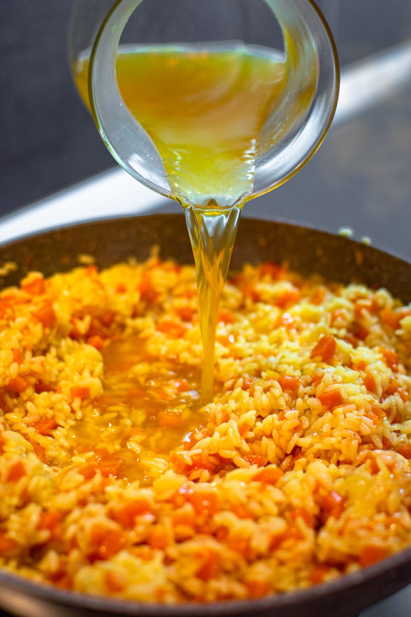 Pouring broth in a pan with rice and carrots
