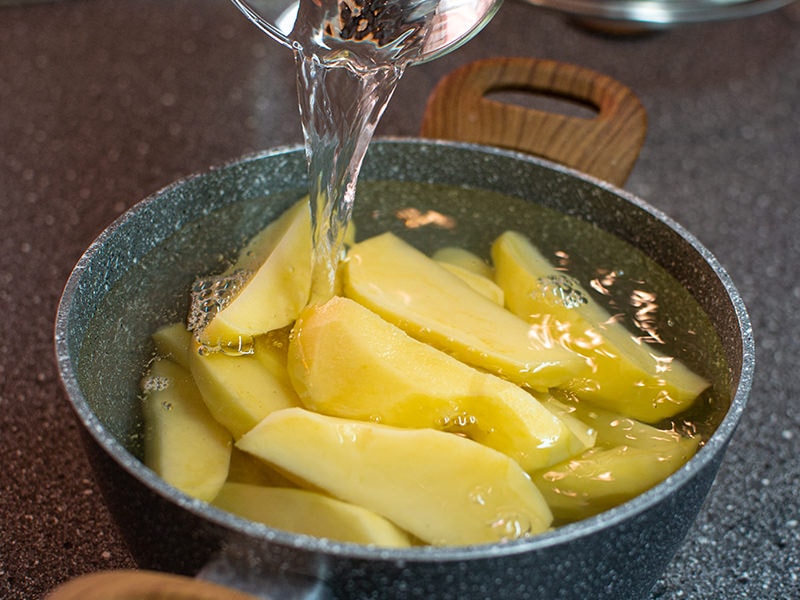 Pouring water over potato wedges in a pan.