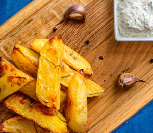 Potato Wedges With Dill Sauce on a wood cutting board.