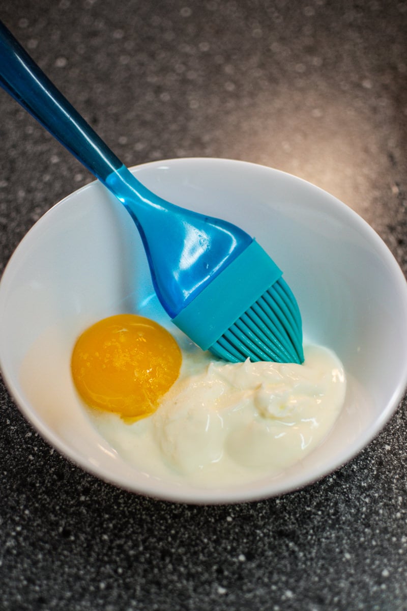 White plate with a raw egg, sour cream and a blue brush in a white plate.