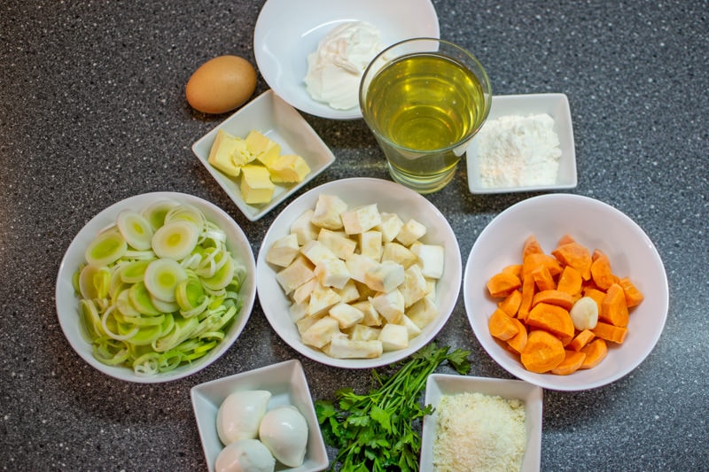 Chopped leek, celery, carrots, onions, and mozzarella on a gray table.