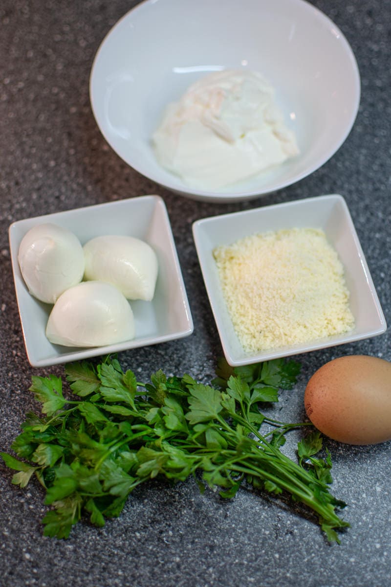 Mozzarella, sour cream, cheese and parsley on a gray table.