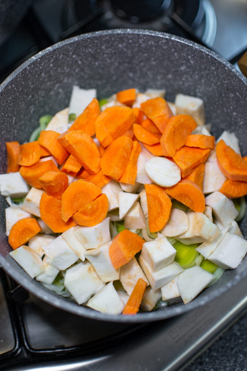 Sliced carrots and celery roots cubes into a gray pan.