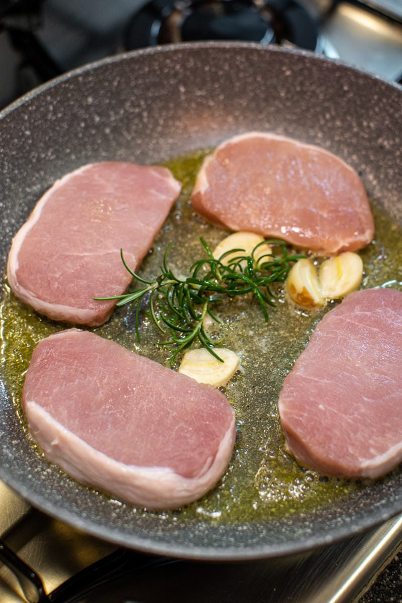 4 Pork Chops on a pan with olive oil, rosemary and garlic cloves.