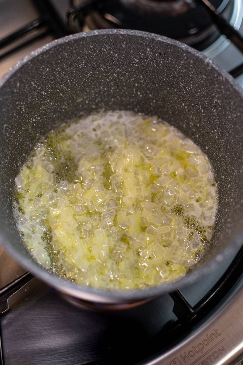 Chopped onions frying in oil into a gray pan.