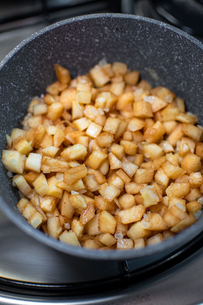 Chopped quince fried into a gray pan on a stove.