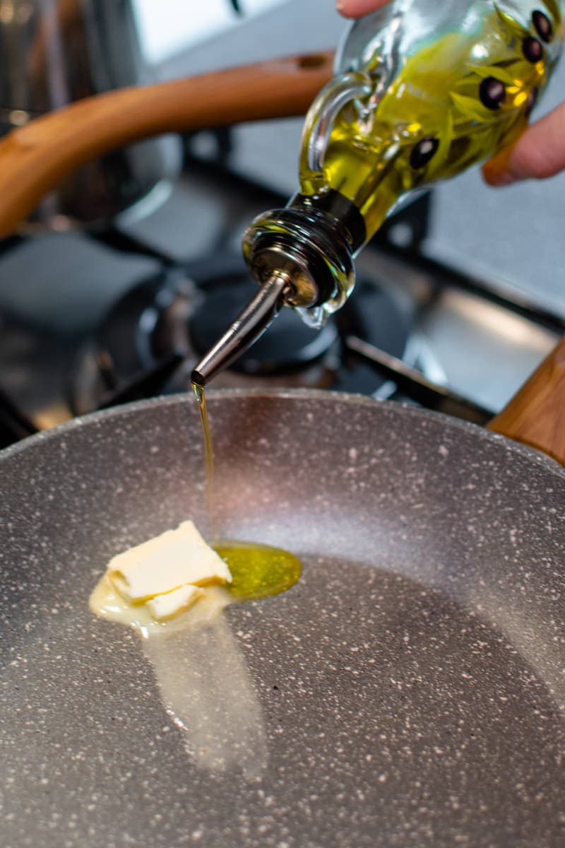 Pouring olive oil above two pieces of button into a gray pan.