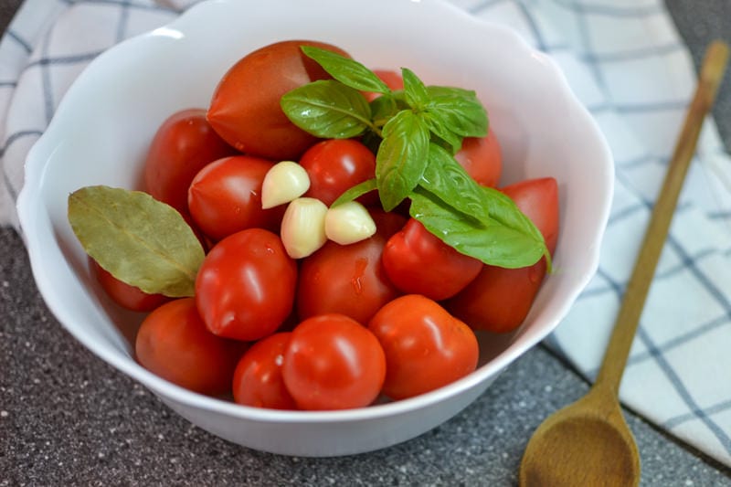 White bowl with fresh tomatoes, garlic, basil & bay laves.