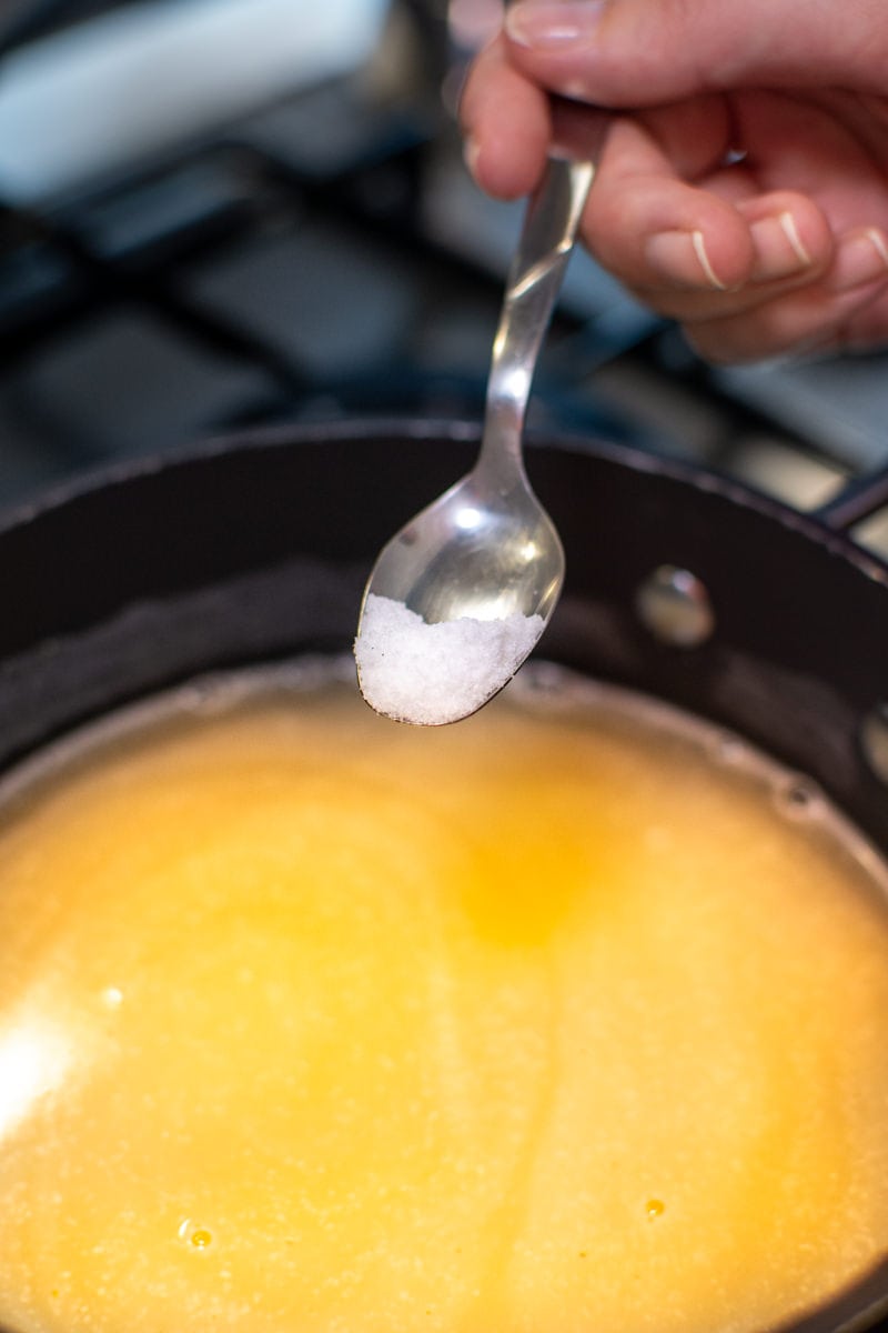 Adding a teaspoon of salt to the creamy corn polenta.
