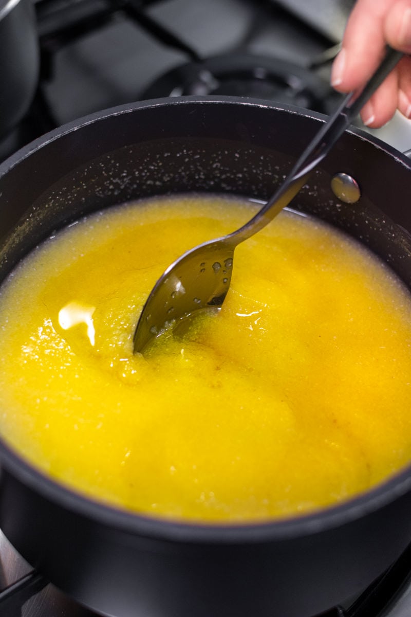Mixing with a spoon a creamy polenta in a dark pan on the stove