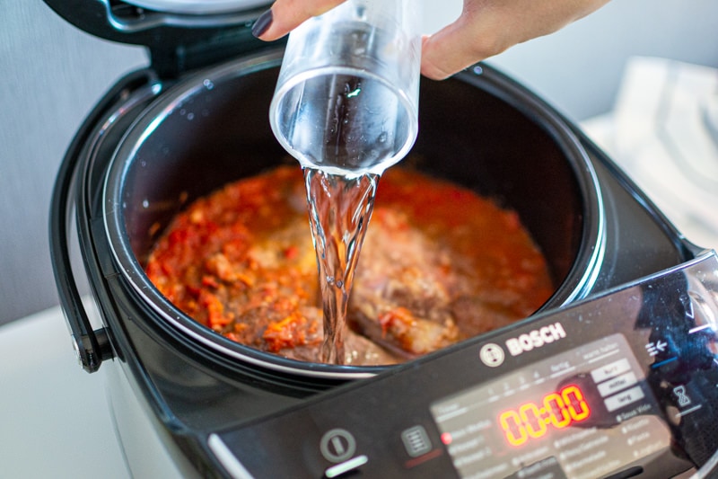 Pouring water into osso buco in a slow cooker.