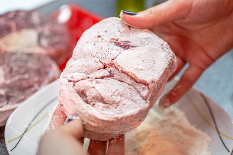 Handing with two hands a veal shank coated with white flour.
