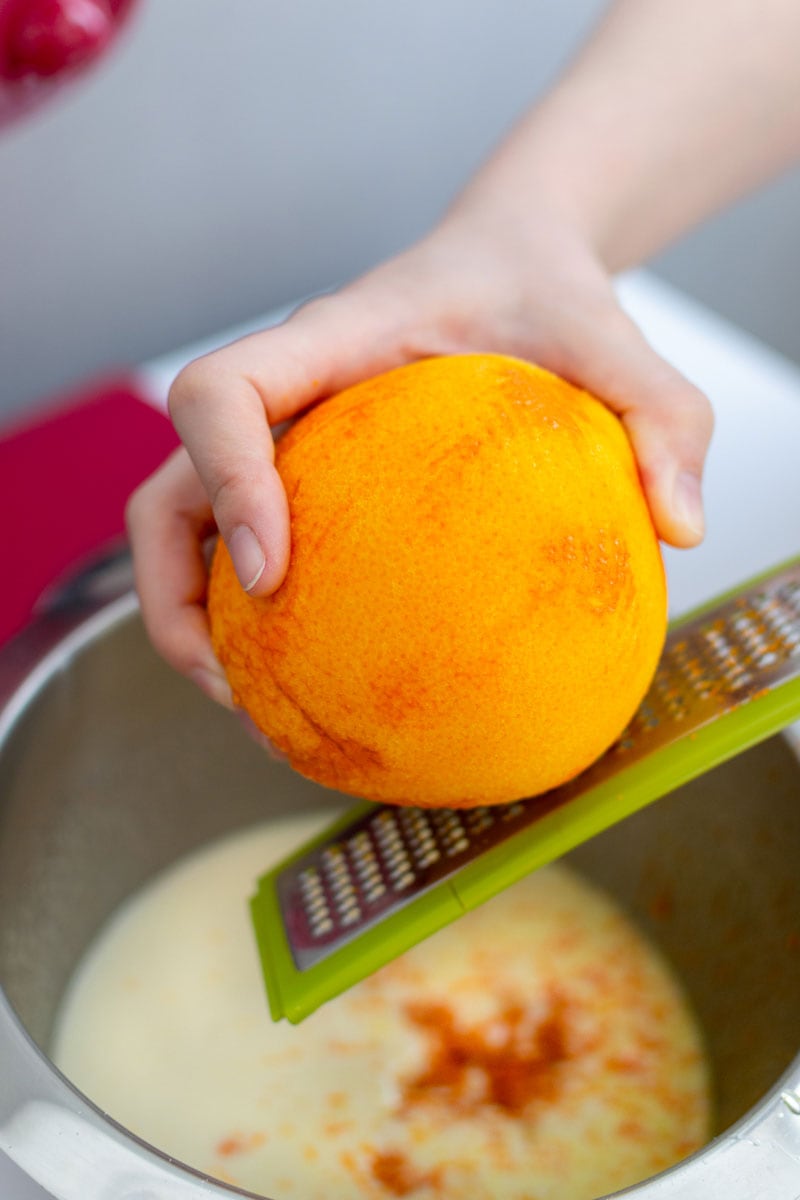 A woman's hand who grate a whole orange.