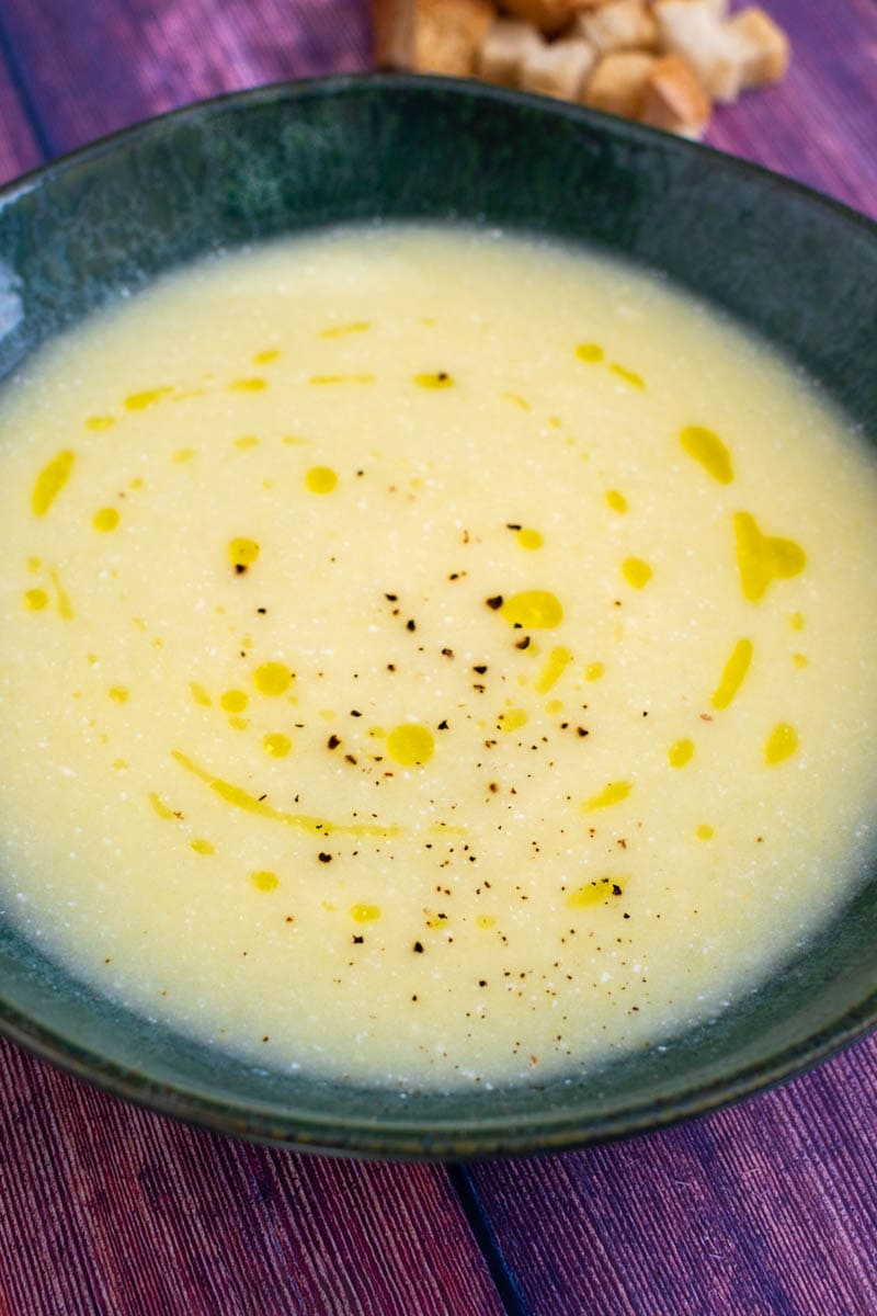 Cauliflower leek potato soup with crackers on wooden table.
