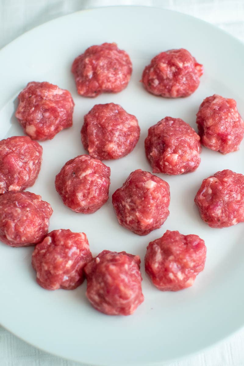 Raw meatballs on a white plate.
