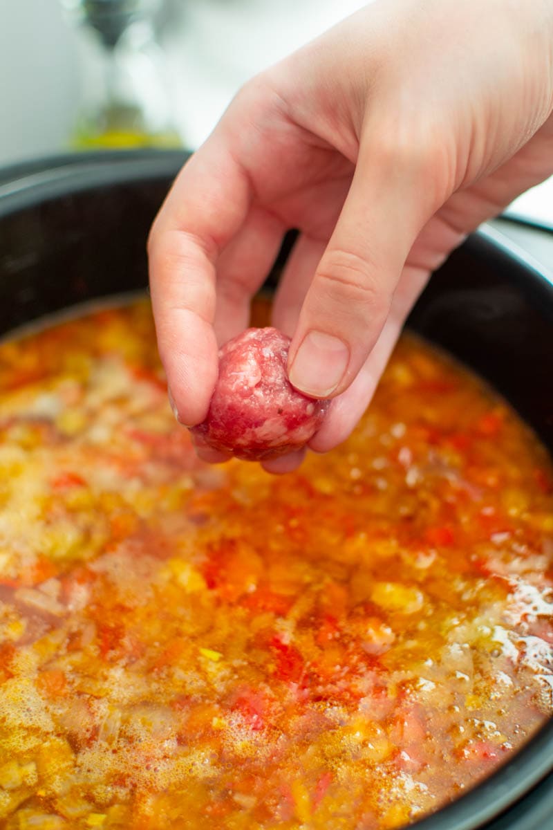 Woman hand adding a meatball into a soup.