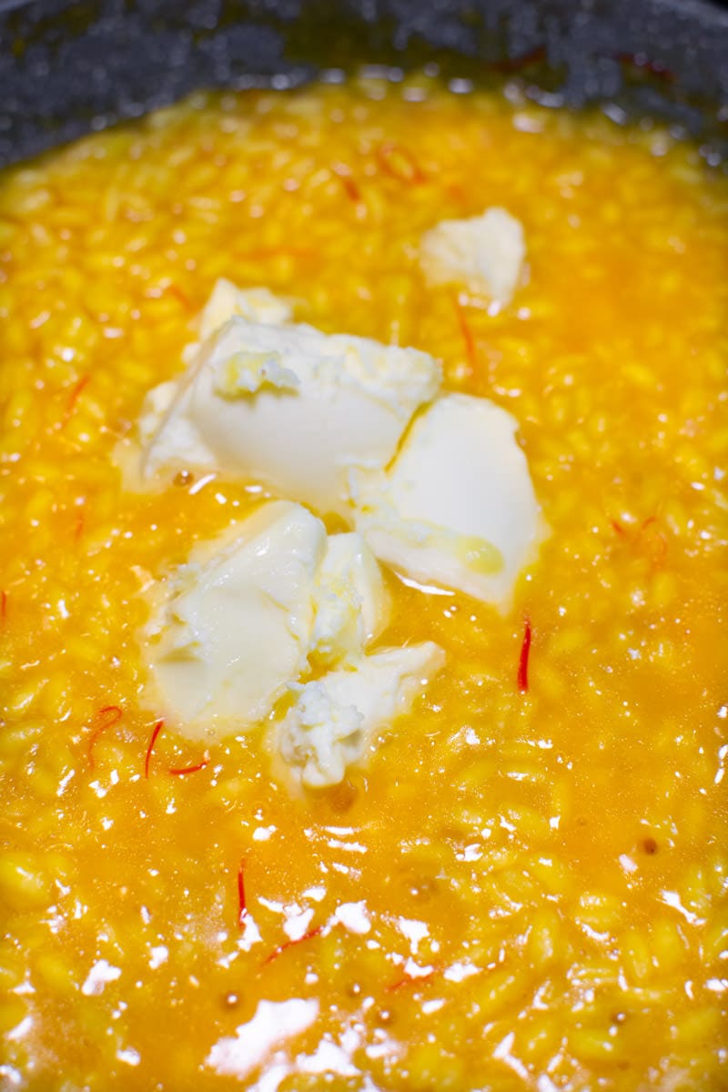 Adding cubes of butter in a creamy yellow risoto allo zafferano.