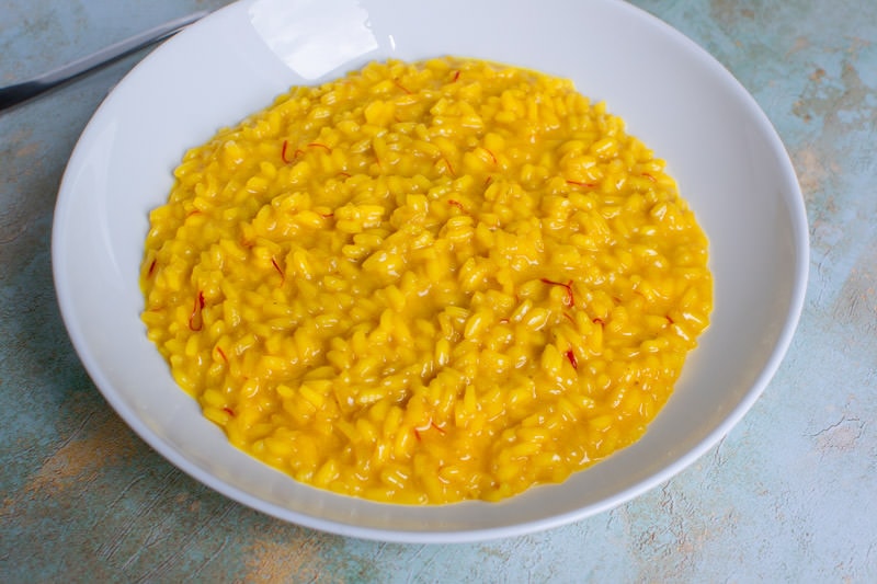 White plate with yellow risotto zafferano with spoon and fork