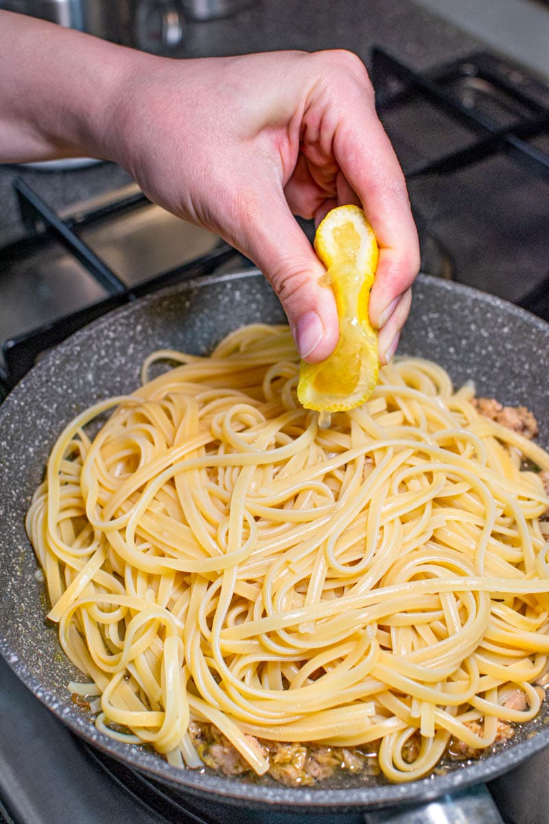 A hand squeezing the lemon over the pasta