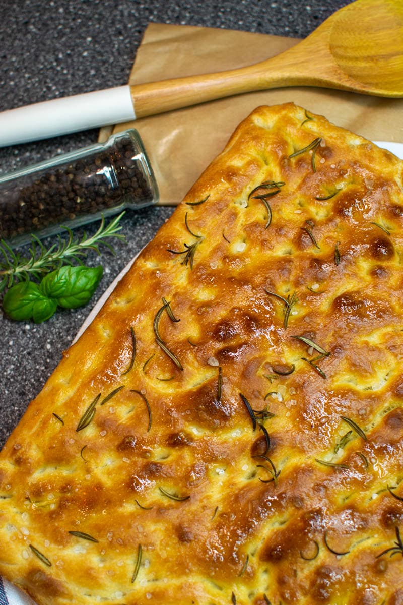 Classic Sicilian focaccia with black pepper and wooden spoon on a table.
