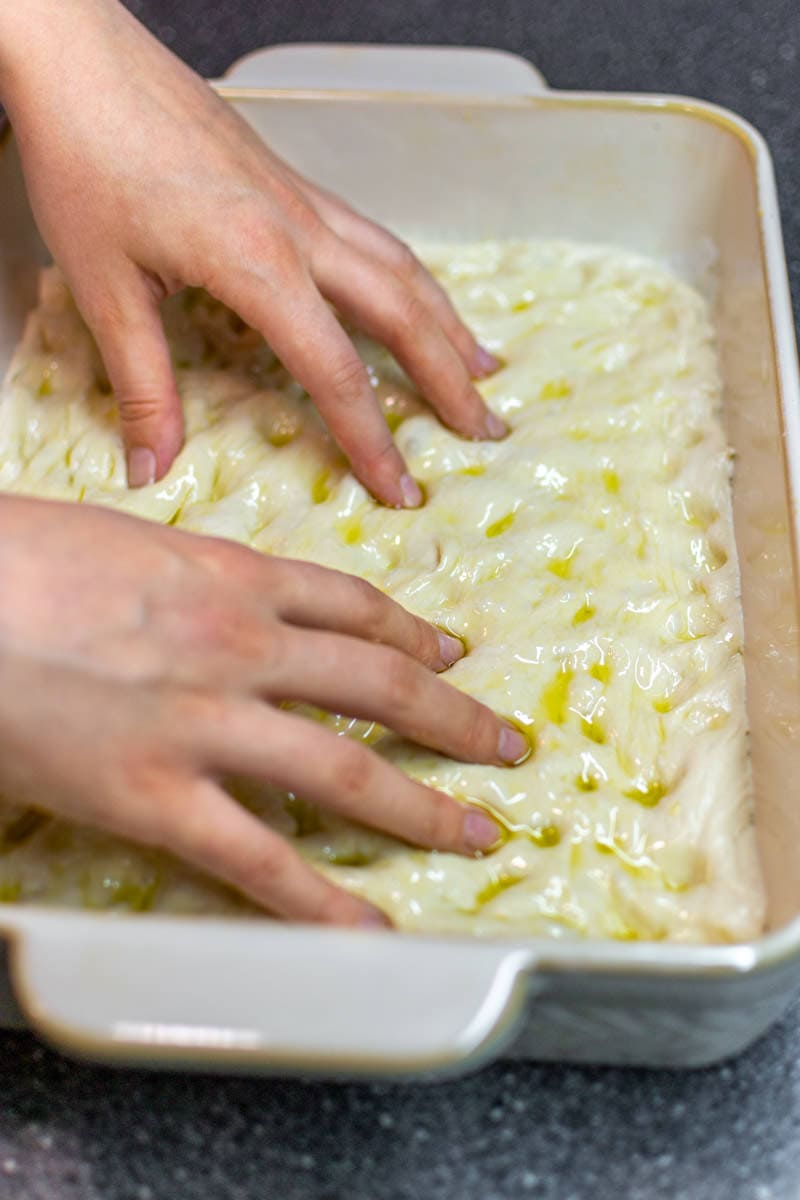Two hands making holes in the italian focaccia bread.