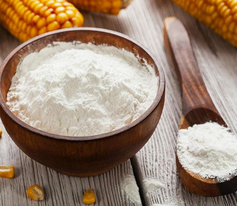 Cornstarch flour on a wooden table with a wooden tablespoon.