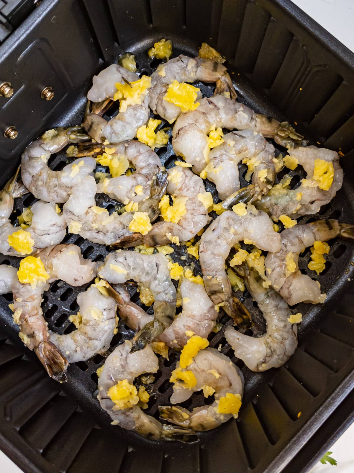 Top view of frozen shrimps with butter and garlic in an air fryer basket.