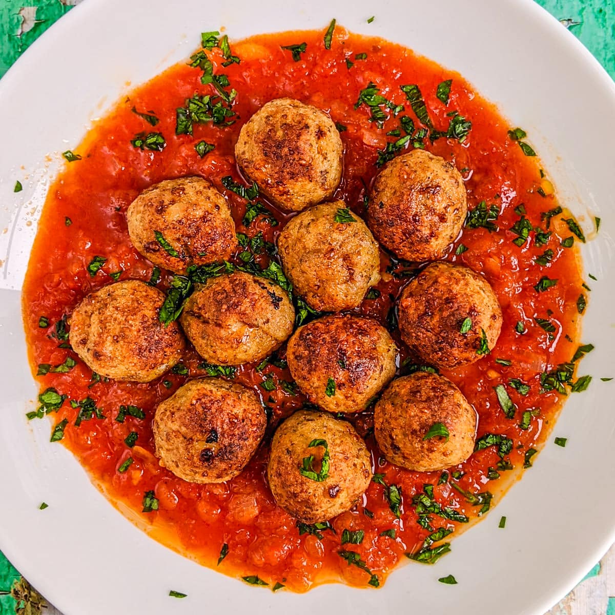 Close top view of a plate with chicken meatballs with tomato sauce.