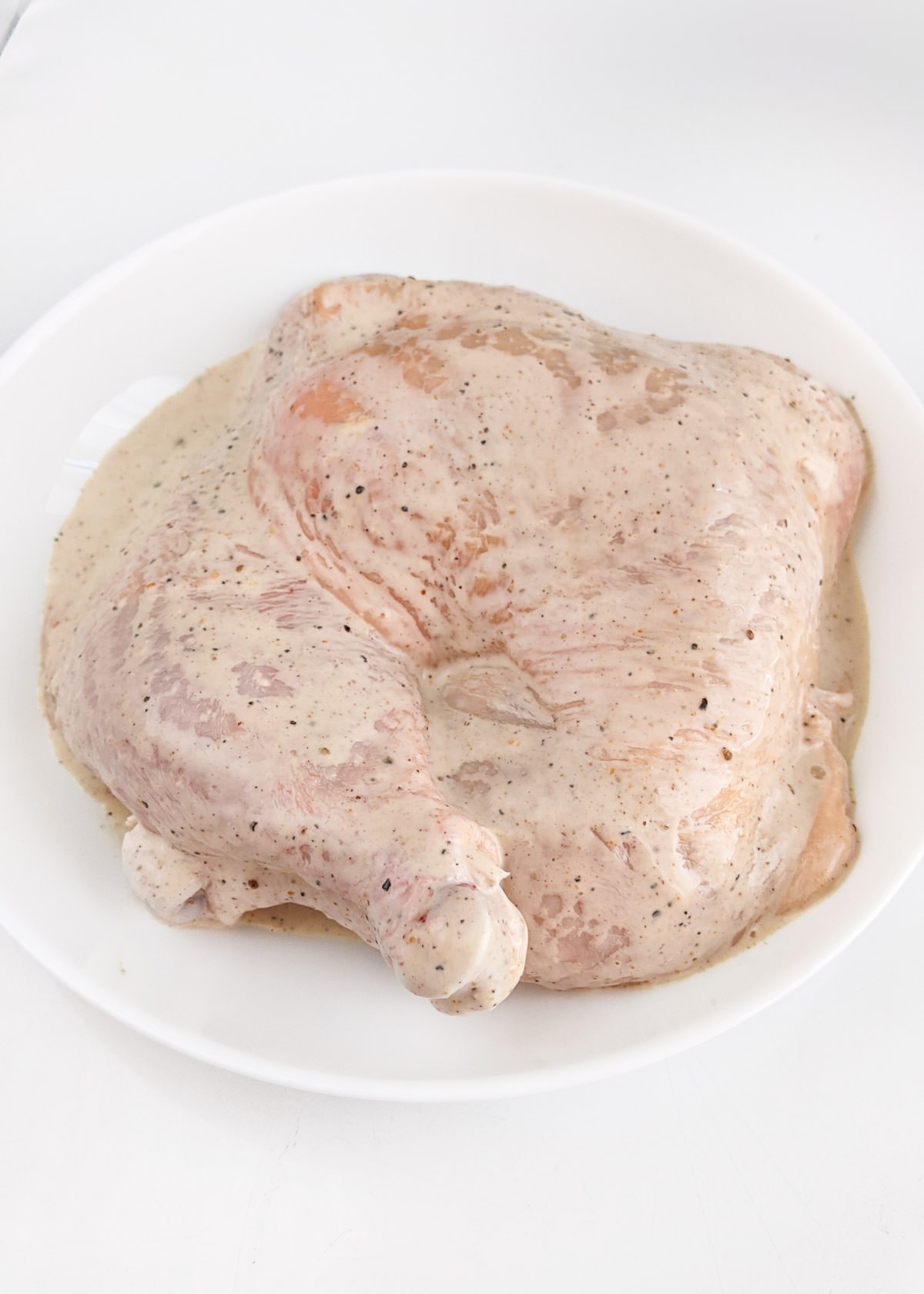 Chicken quarters in marinade in a white plate.