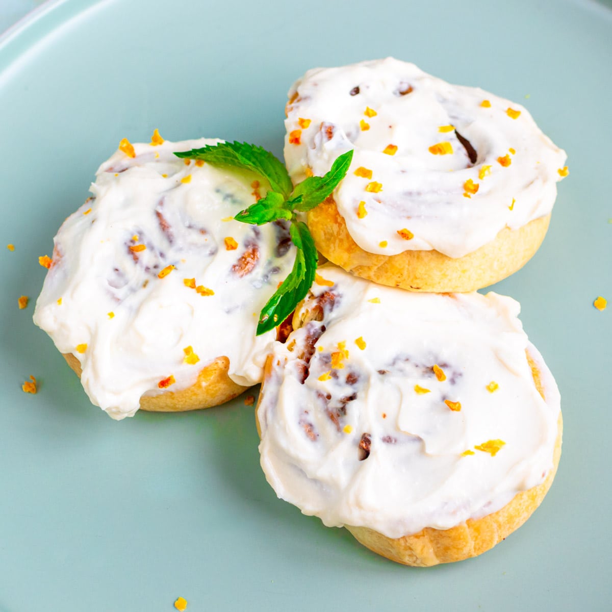 Close look of 3 cinnamon rolls sparkled with orange zest and decorated with mint leaves.