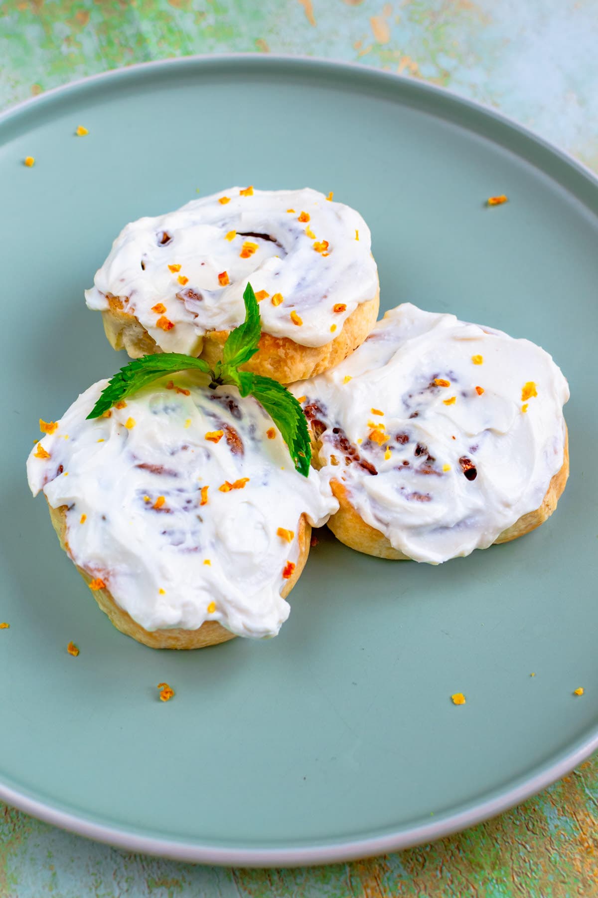 Top view of cinnamon rolls with cream, orange zest and mint leaves.
