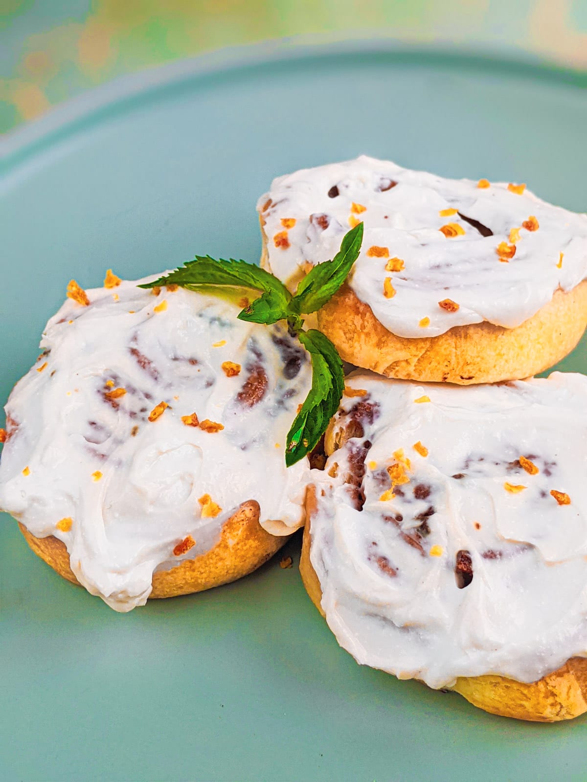 Close look of 3 cinnamon rolls with orange zest and mint leaves.