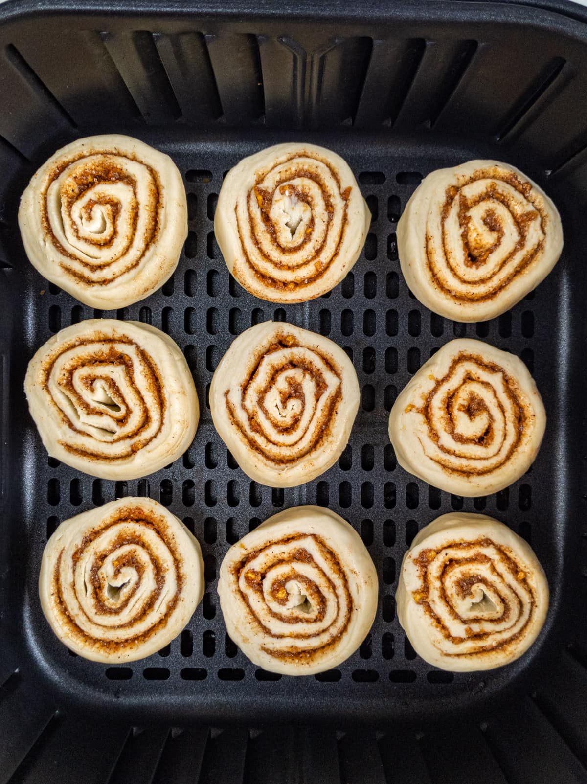Top view of 9 cinnamon rolls in an air fryer basket.
