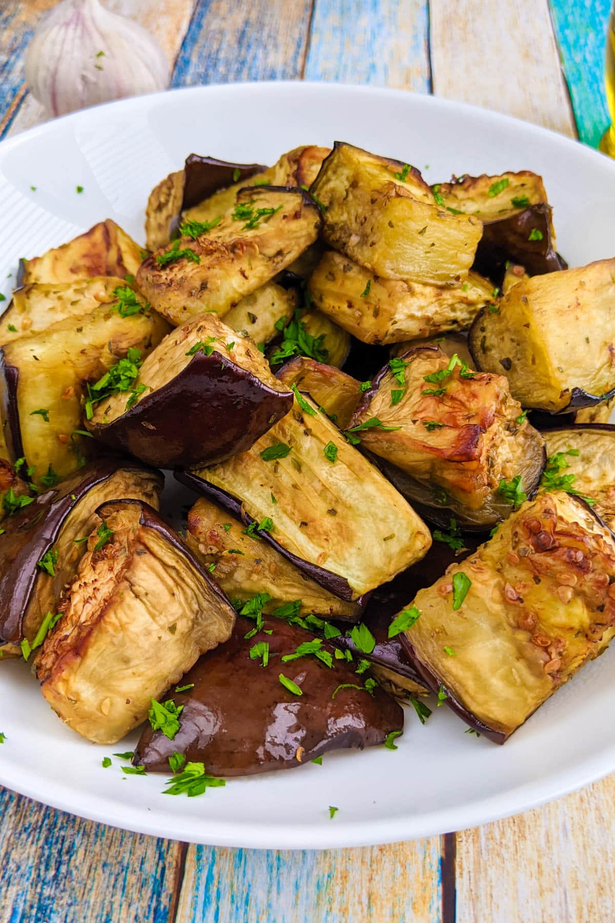 Eggplants bites with copped parsley on a white plate.