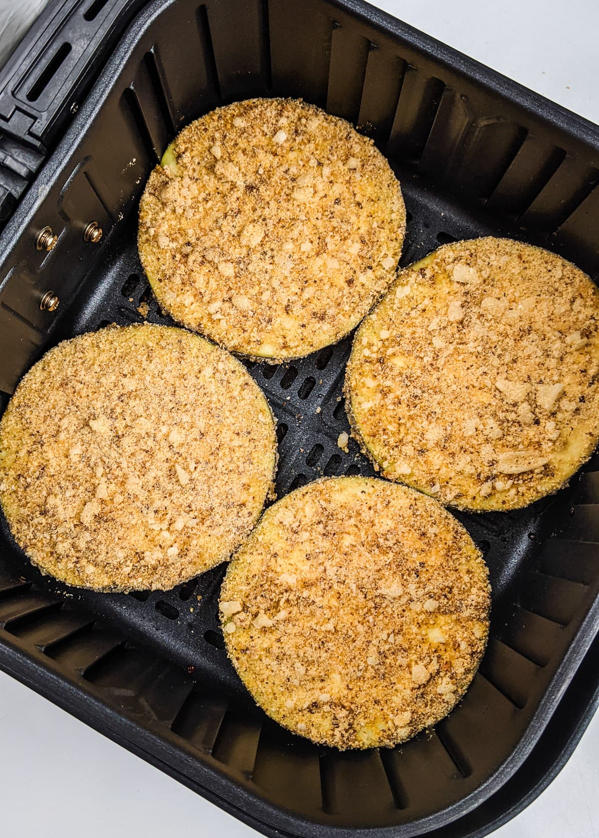 Close look of eggplant slices crusted in breadcrumbs in an air fryer basket.