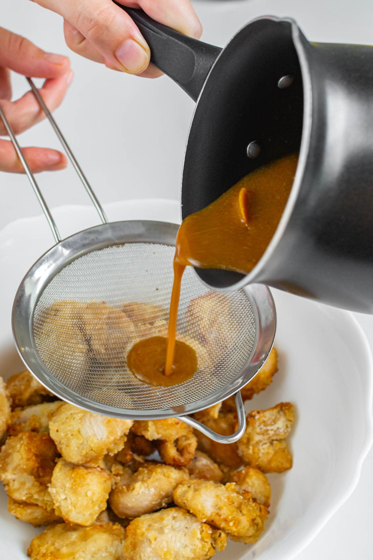 Pouring orange sauce over air fried chicken breast pieces.