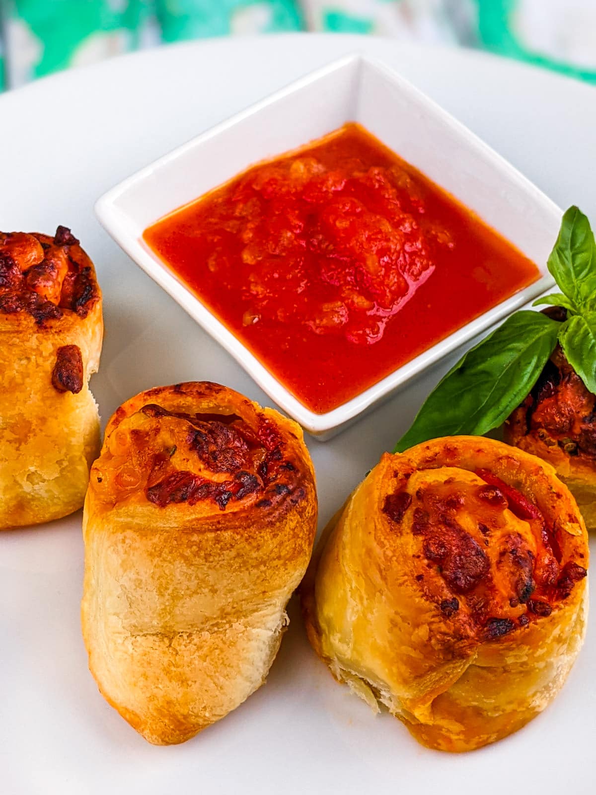 4 pizza rolls with basil leaves and tomato sauce on white plate.