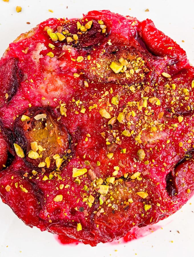 Top view of a juicy yogurt plum cake topped with plum and crushed pistachios.