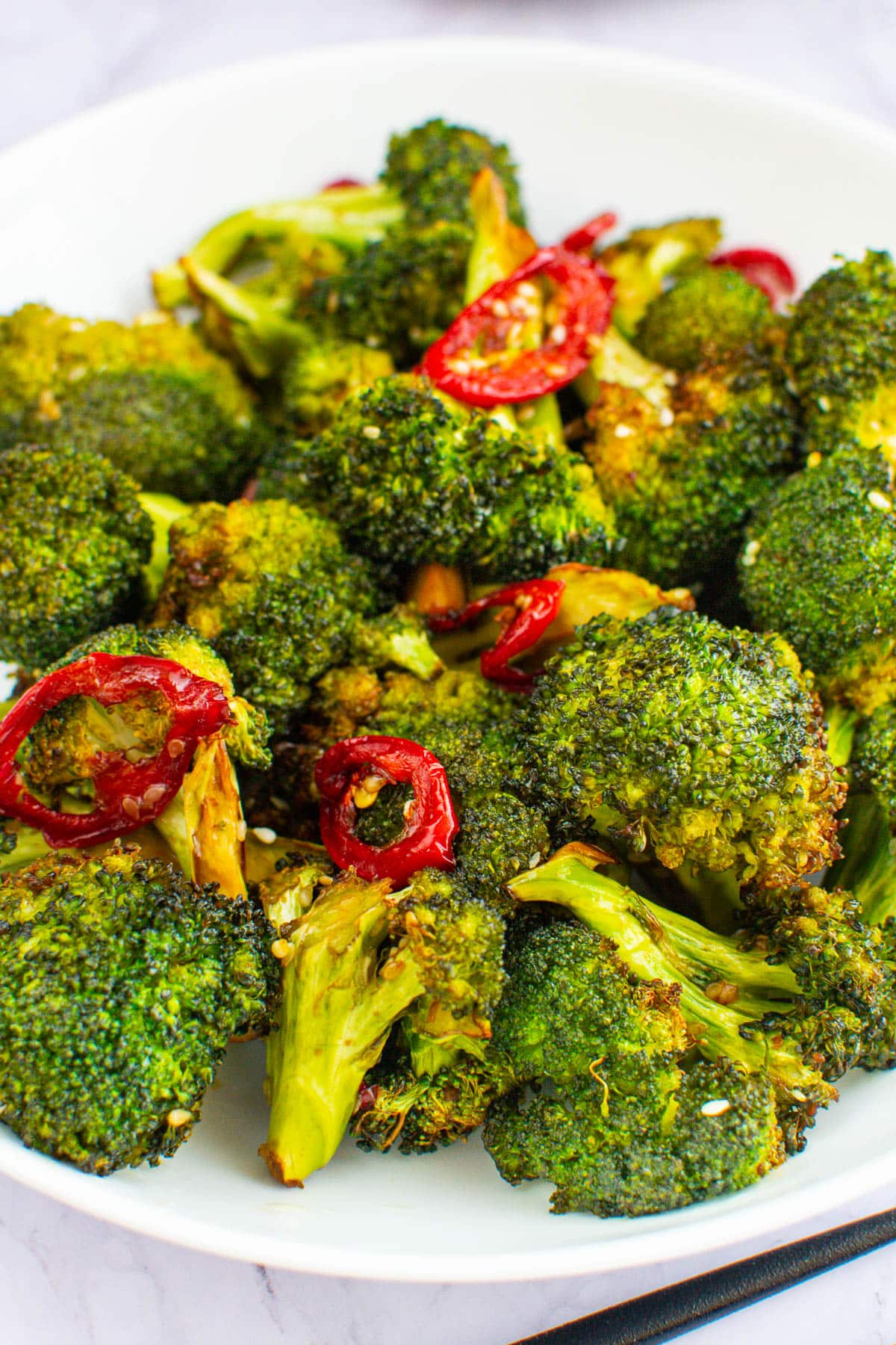 Broccoli with red hot pepper and sesame seeds on a white plate.