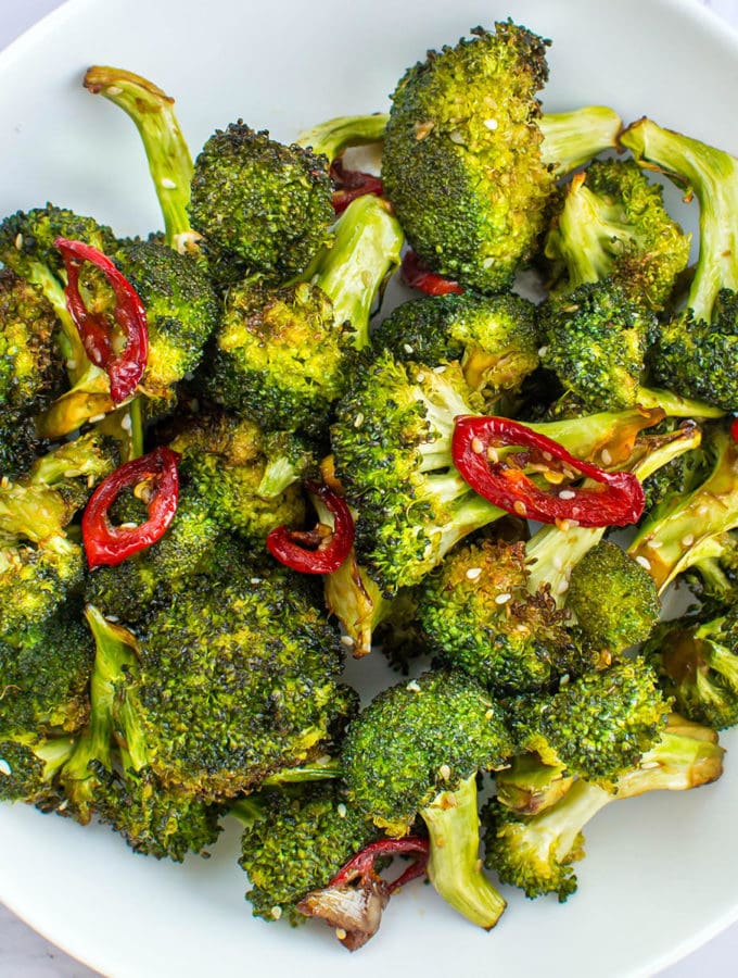 Broccoli with red hot pepper and sesame seeds on a white plate.