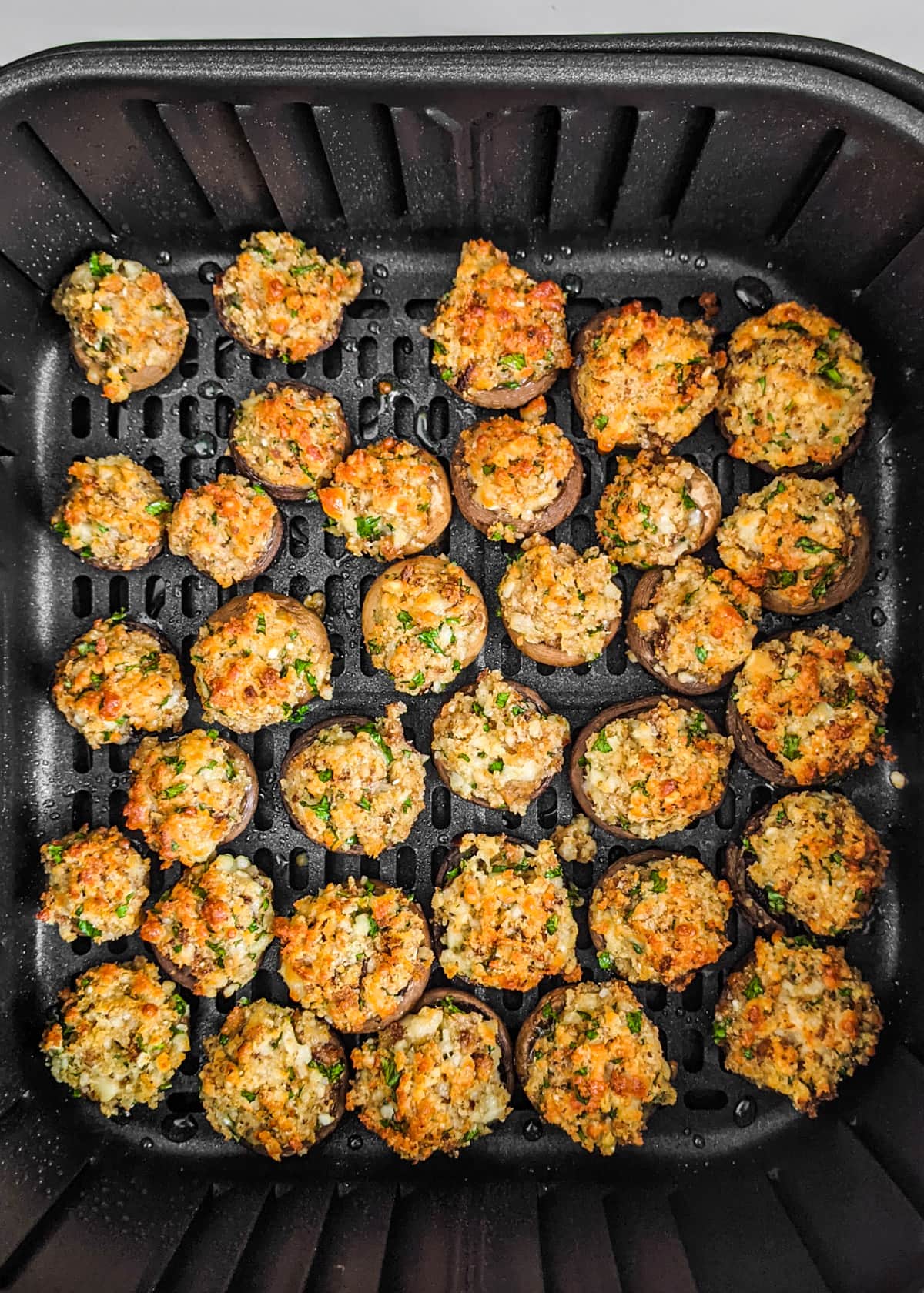 Air fryer basket with cooked stuffed mushrooms.