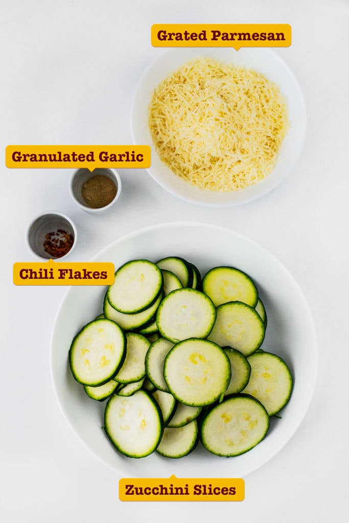 Simple ingredients for parmesan zucchini chips on white table.