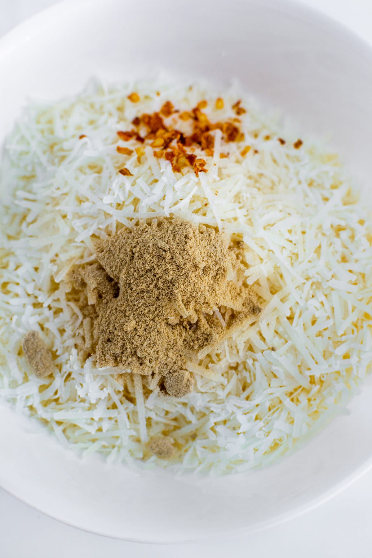 Close look of grated parmesan with granulated garlic and chili flakes on a white plate.