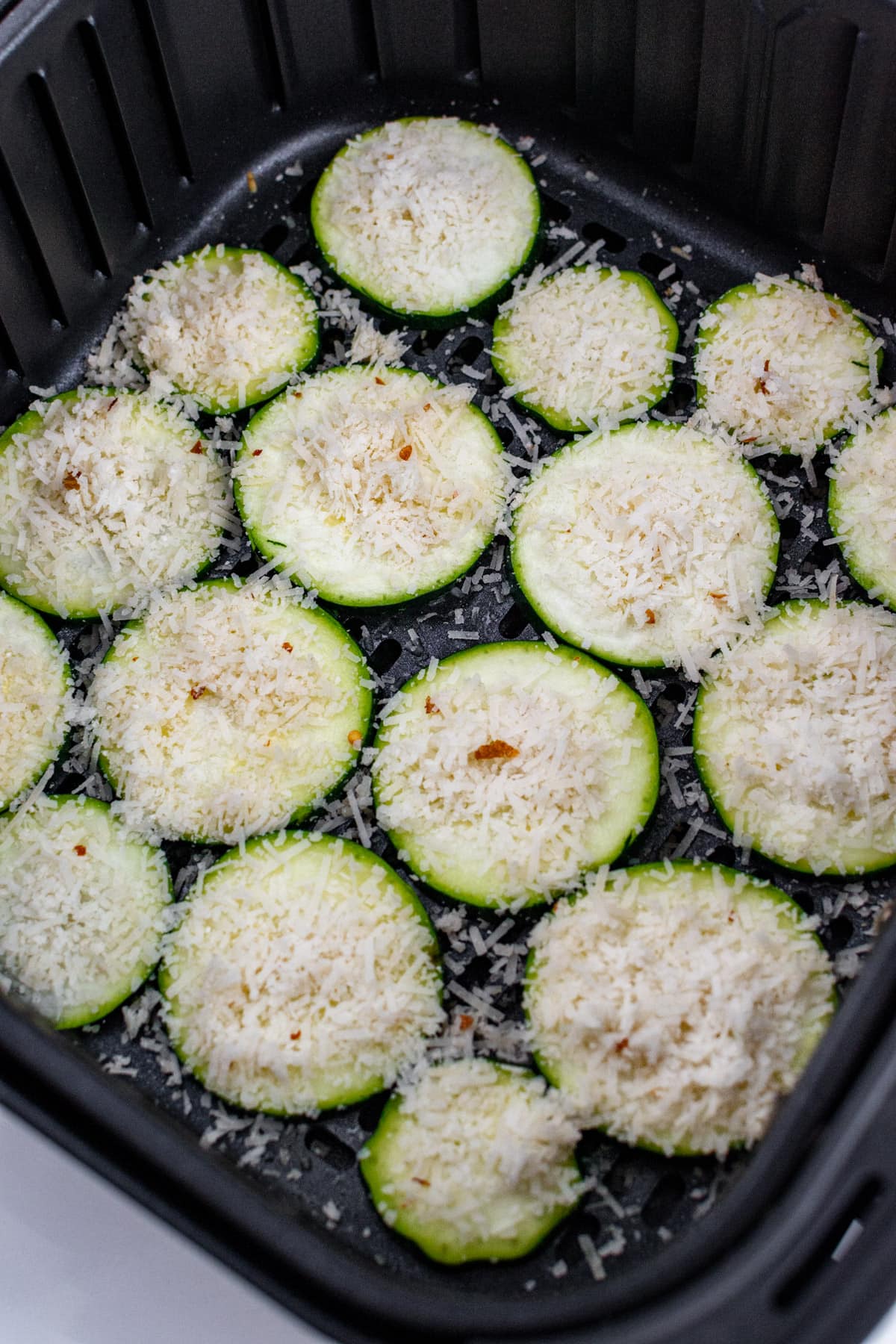 Zucchini slices of grated parmesan and chili flakes in an air fryer basket.