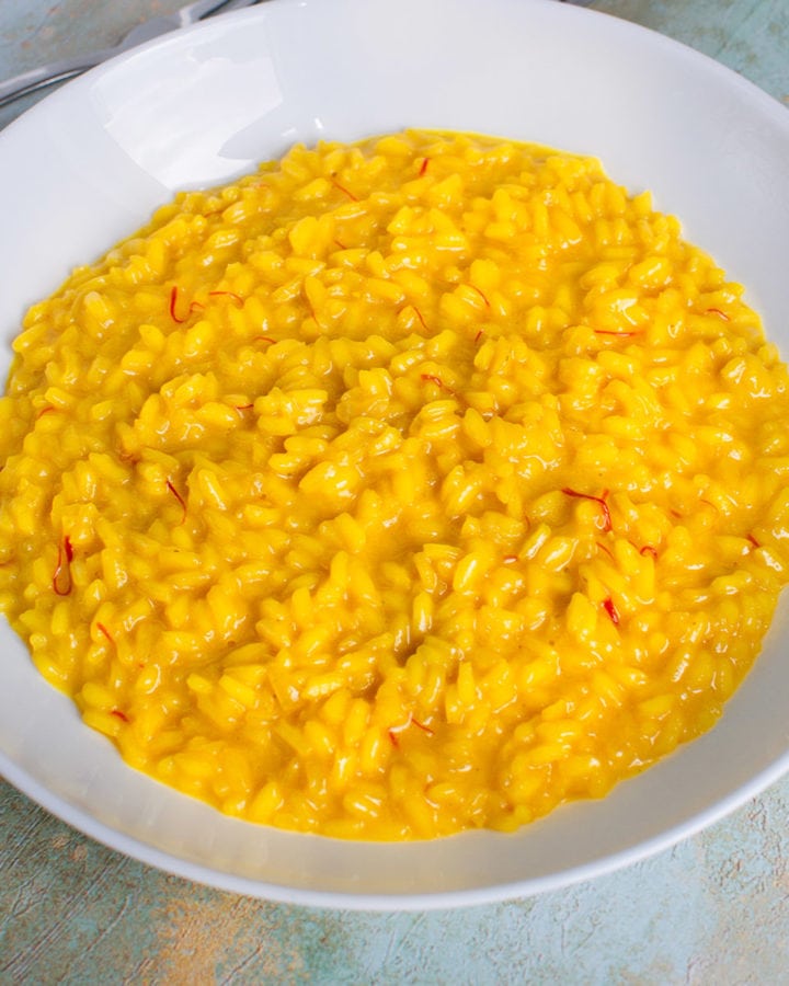 White plate with yellow risotto zafferano with spoon and fork.